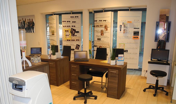 Modernes Augenoptiker-Geschäft mit Brillenauswahl, Beratungstischen und Computerarbeitsplätzen.